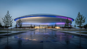 Модерната фасада на Arena Burgas, осветена в синьо вечерта.